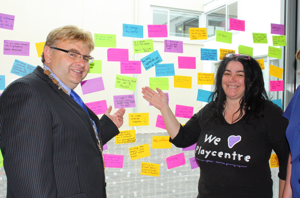 Lower Hutt Mayor Ray Wallace and Hutt Play Centre volunteer, Mishi Berecz, with the wall of Post It notes written by volunteers who attended the Mayoral thank you breakfast at the Dowse on 5 December.