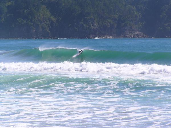 A surfer pulling into a left hand barrel in front of Hot Water Beach Rocks at the South end.