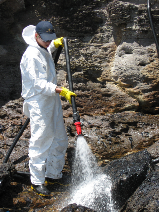 New Zealand Defence Force personnel use salt water to flush oil off rocks at the base of Mt Maunganui.