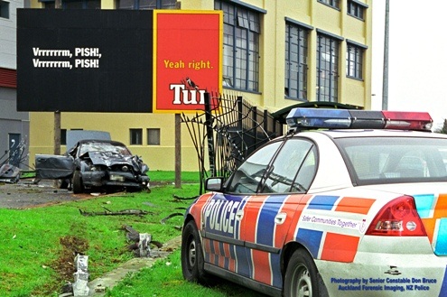 Driver loses control of car and careers through a fence into a billboard. Police car arrives at scene.