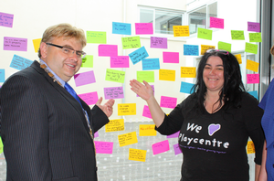 Lower Hutt Mayor Ray Wallace and Hutt Play Centre volunteer, Mishi Berecz, with the wall of Post It notes written by volunteers who attended the Mayoral thank you breakfast at the Dowse on 5 December.