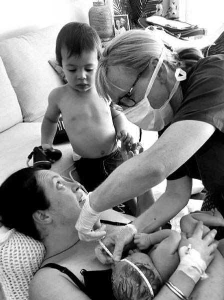 2 year old Rory watches as midwife Megan Hurst measures the head of his new sister Kora resting on mum Ruth